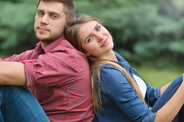 Young adult couple siting back in back in nature — Stock Photo, Image