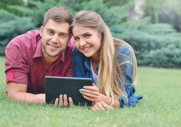 Happy couple lying in the park using tablet pc together — Stock Photo, Image