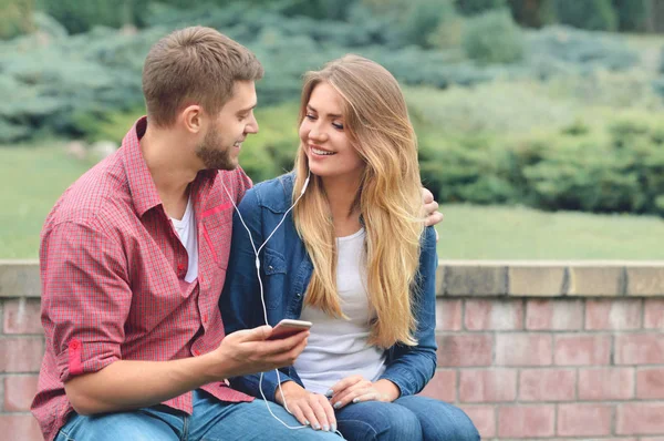 Paar luisteren naar de muziek met earbuds van een slimme telefoon in een park. — Stockfoto