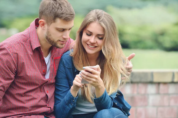 Young couple looking at a smartphone together on a bench in the park — Stock Photo, Image