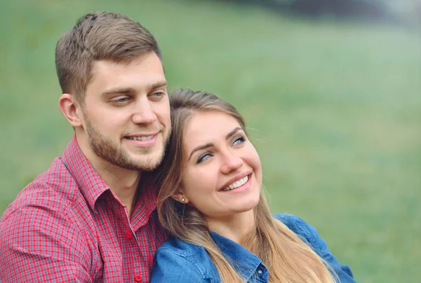 Portrait of romantic couple sitting on the grass, look ahead and smile — Stock Photo, Image