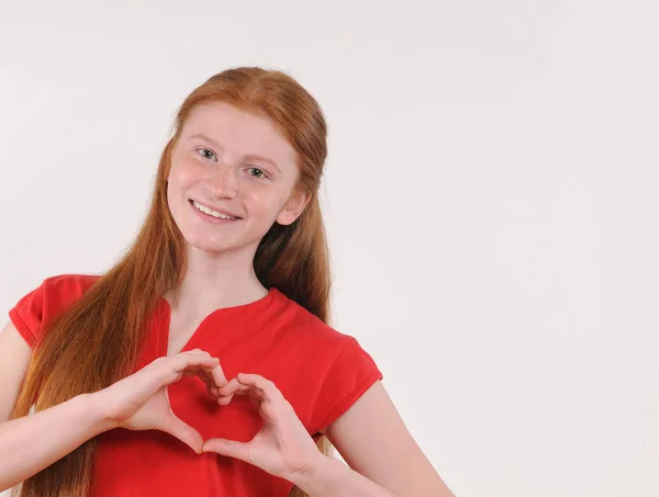 Junges Mädchen mit rotem Haar zeigt Herzform mit Händen auf grauem Hintergrund — Stockfoto