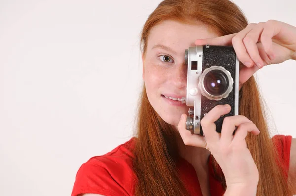 Молодая рыжая девушка держит винтажную камеру на сером фоне — стоковое фото