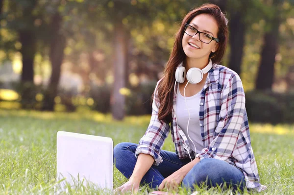 坐在公园的草地上的笔记本电脑上工作的女学生 — 图库照片