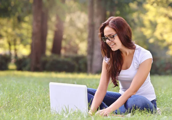 Dizüstü bilgisayarda çalışma ve oturma öğrenci kız parkta çim üzerinde bacak bacak