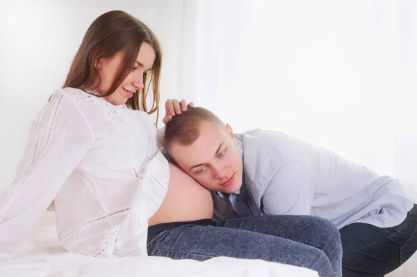 Handsome man is listening to his beautiful pregnant wife's tummy — Stock Photo, Image