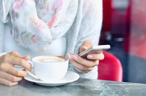 Xícara de café e mãos de mulheres jovens com smartphone no café — Fotografia de Stock