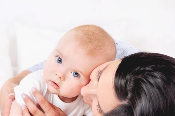 Mama przytula syna na białym łóżku — Zdjęcie stockowe