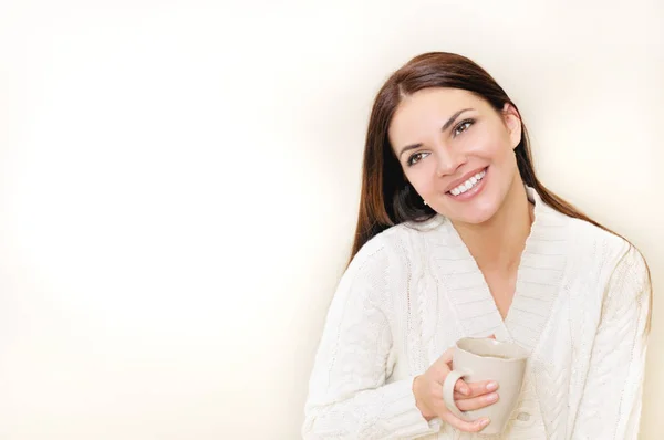 A happy woman with a cup of tea wears a white sweater smiling — Stock Photo, Image