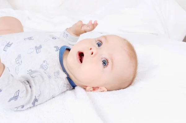 Funny baby infant child with blue eyes lying on the bed — Stock Photo, Image