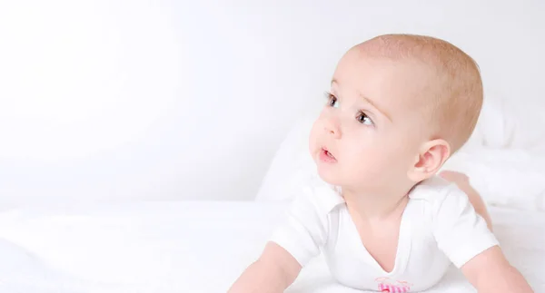 Cute baby with beautiful brown eyes lying in white bed — Stock Photo, Image