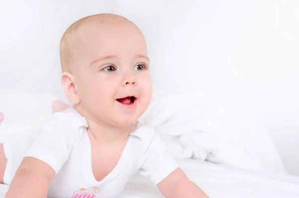 Happy child lie on white bed and smile — Stock Photo, Image