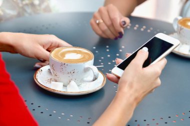 İki kahve fincanı ve elleri açık kafe smartphone olan genç kadın