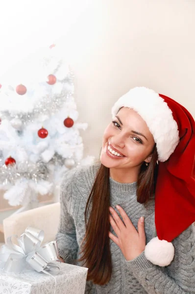 Feliz joven en Santa Sombrero regocijarse por el regalo al lado del árbol de Navidad —  Fotos de Stock