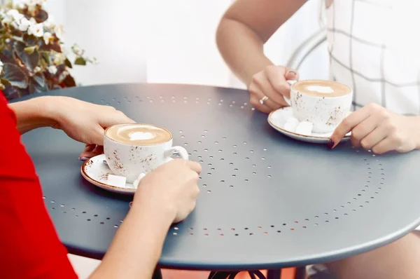 Две чашки кофе и руки молодых женщин в кафе на открытом воздухе — стоковое фото
