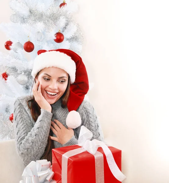 หญิงสาวที่มีความสุขในหมวกซานต้า ยินดีที่ของขวัญข้างต้นคริสต์มาส — ภาพถ่ายสต็อก