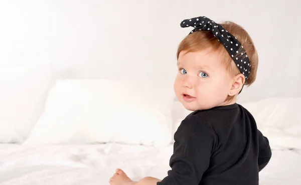 Χαριτωμένο μωρό κορίτσι ντυμένο με ένα μαύρο φόρεμα σε φόντο λευκό κρεβάτι — Φωτογραφία Αρχείου