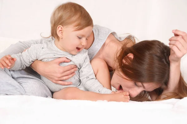 Mãe brincar com sua filha no fundo da cama branca — Fotografia de Stock