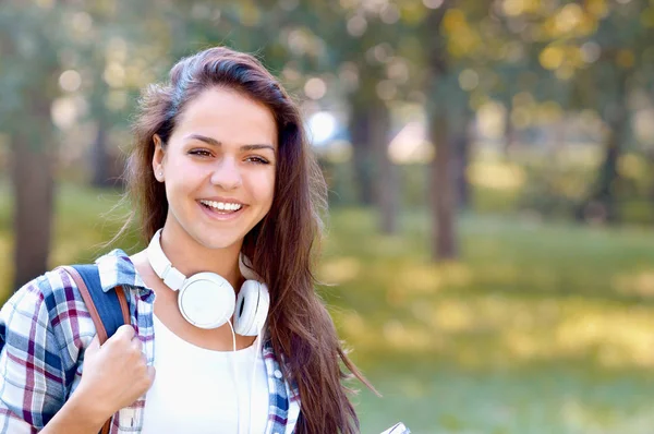 愉快的学生女孩与背包和耳机微笑在夏天公园 — 图库照片