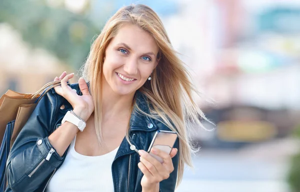 Jovem sorrindo mulher com sacos de compras segurar telefone celular — Fotografia de Stock