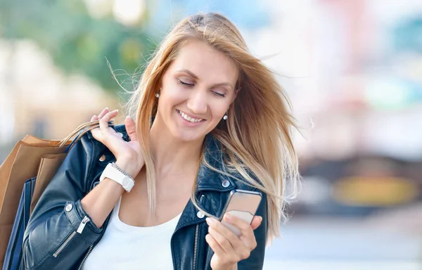 Jovem sorrindo mulher com sacos de compras olhar para o telefone celular — Fotografia de Stock