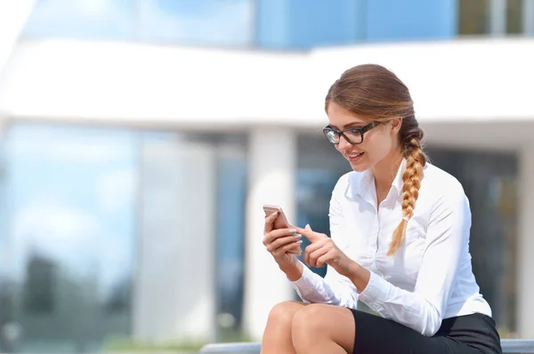 मुस्कुरा रही युवा महिला मोबाइल फोन पर पाठ संदेश पढ़ने के बाहर बैठी — स्टॉक फ़ोटो, इमेज