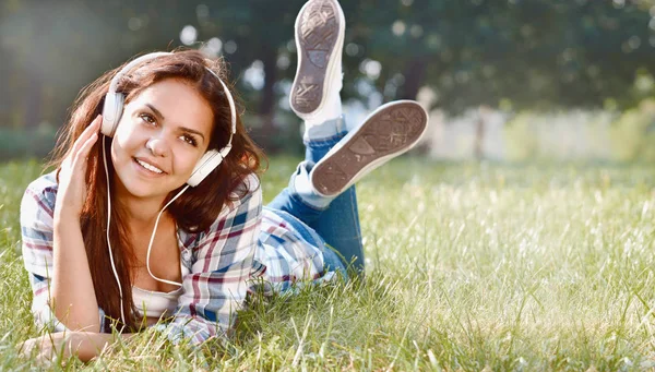 Portrait of young girl listening music lying at the grass — Stock Photo, Image