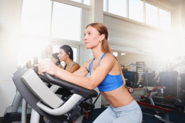Group of four people in the gym, exercising their legs doing cardio training. Fitness young women on gym bike