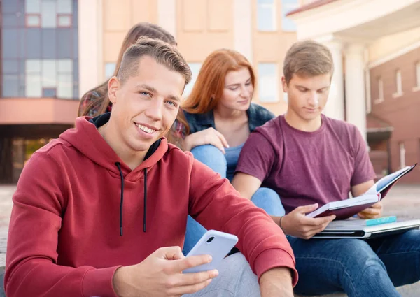 在大学附近的楼梯上 一个笑得很开心的少年拿着手机和一群学生对视 教育概念 — 图库照片