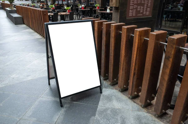 Blank white outdoor advertising stand/sandwich board mockup template. Clear street signage board placed by an outdoor dining area of a restaurant. Background texture of standee on the et.