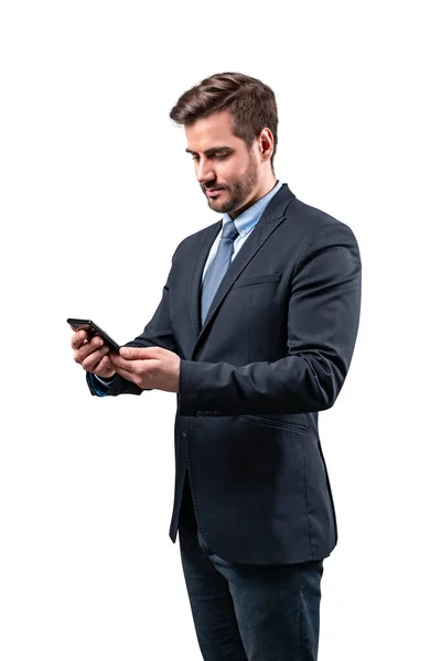 Sorridente giovane uomo guardando il suo smartphone mentre messaggistica di testo isolato su sfondo bianco — Foto Stock