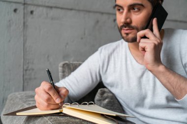 Telefonda konuşan ve koltukta notlar alan bir adam.