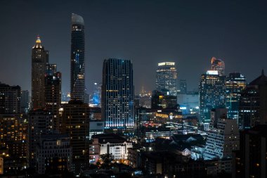 Gece vakti Bangkok siluetinin panoramik görüntüsü. Tayland 'ın aydınlatılmış şehir merkezi. Çağdaş binaların dış yüzeyi camdan..