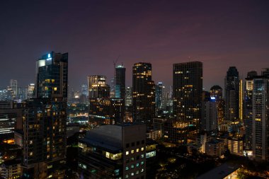 Gece vakti Bangkok siluetinin panoramik görüntüsü. Tayland 'ın aydınlatılmış şehir merkezi. Çağdaş binaların dış yüzeyi camdan..