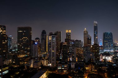 Gece vakti Bangkok siluetinin panoramik görüntüsü. Tayland 'ın aydınlatılmış şehir merkezi. Çağdaş binaların dış yüzeyi camdan..