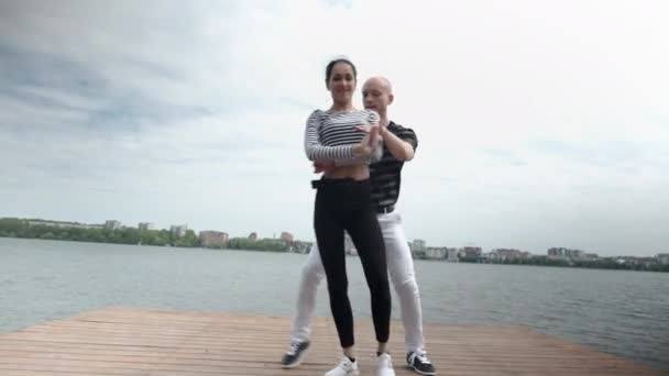 O casal apaixonado dança social bachata pier no lago, horizonte da cidade — Vídeo de Stock
