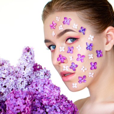 Beyaz arka planda güzel bir kızın yüzünde bahar leylağı çiçeği
