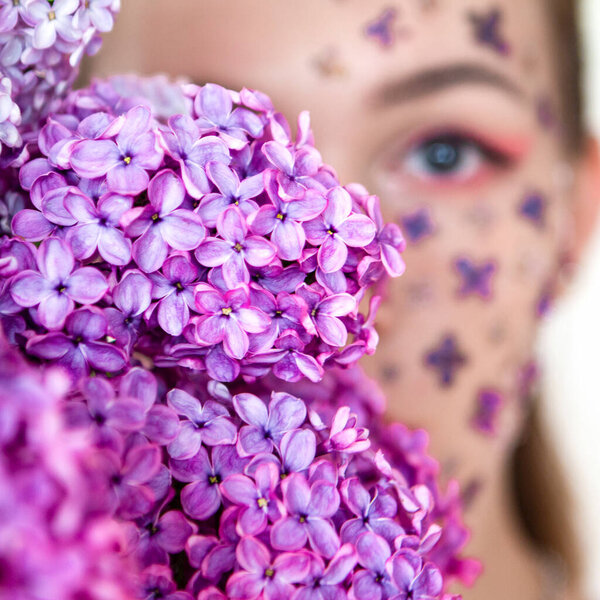 spring lilac flower on the face of a beautiful girl on a white background