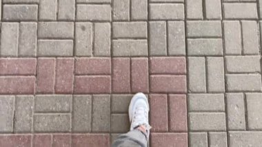 Geniş gri kotlu kadın bacakları ve beyaz spor ayakkabıları üzerinde belli aralıklarla yumurtadan çıkan taş bir fayans üzerinde yürür..