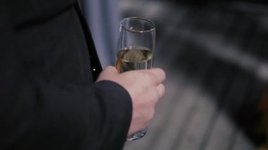 Mavi ceketli bir adam elinde şampanya dolu bir bardak tutuyor.