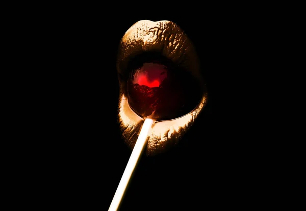 Labbra dorate con un lecca-lecca rosso isolato su fondo nero. Sensuale bocca sexy con caramelle, concetto di godimento di belle labbra femminili. Rossetto per feste speciali — Foto Stock