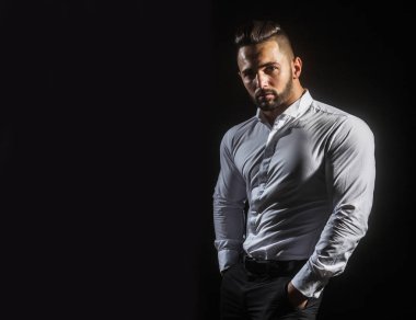 Ciddi adam ellerini onun pantolon ya da pantolon ceplerinde tutar. Tıraşsız genç iş adamı ile spor vücut Beyaz gömlekli. Adam atletik vücut ile kendine güvenen görünümünü. Erkek model siyah izole
