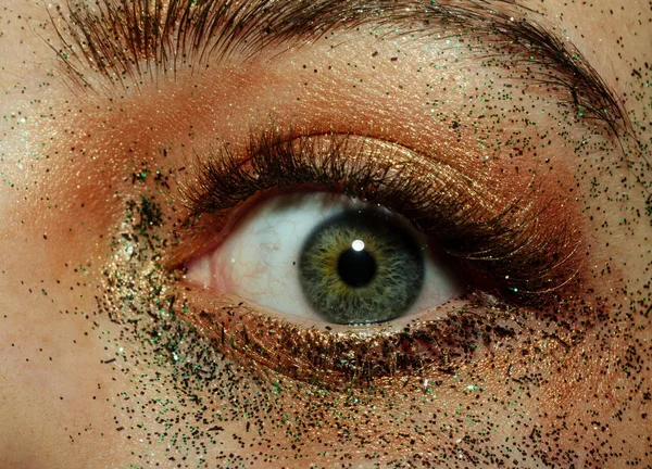 Ojo inusual con maquillaje creativo con destellos. Abre los ojos verdes de cerca. Pupila femenina y lente sana, vista y salud ocular. Oro y brillo en cosmetología — Foto de Stock