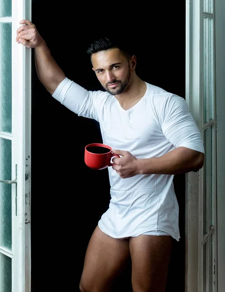 Morgenkaffee. attraktiver Mann in Unterwäsche mit einer Tasse Kaffee in der Hand. Küche und Frühstück. Bärtiger Mann im weißen T-Shirt trinkt Kaffee in seinem Haus — Stockfoto