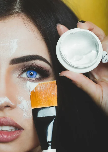 Cosméticos para la cara. Hermosa cara femenina con cepillo o borla para el cuidado cosmético de la piel con crema de cerca. Chica morena con ojos azules — Foto de Stock