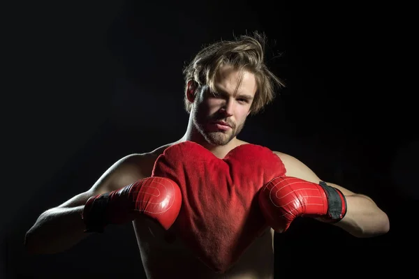 Corazón de boxeador. Hombre atractivo en guantes rojos de boxeo sostiene almohada en forma de corazón para el Día de San Valentín. En el amor boxeador sobre fondo negro — Foto de Stock