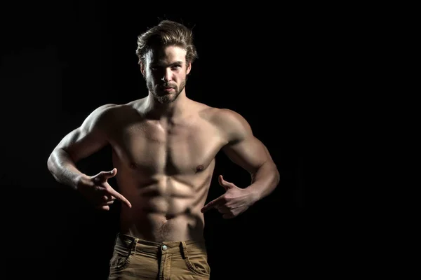 Man is pointing at his naked athletic belly. Muscles of young strong bearded guy. Attractive sexy man
