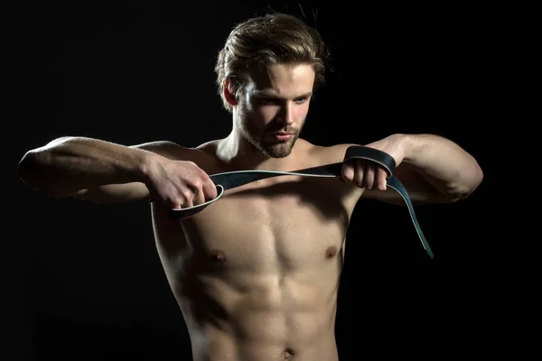 Belt is in the hands of naked man. The guy does exercises for hands with leather belt. Sexy model for men's accessories. Concentration and meditation in the gym — Stock Photo, Image