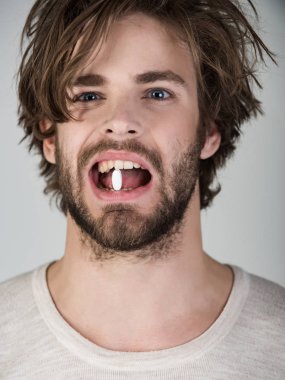 Adam şifa hap dişlerini içinde tutuyor. Hasta genç çekici ağız beyaz tıbbi tablet adam sakallı. Tedavi ve sağlık, tıp ve eczacılık kavramı