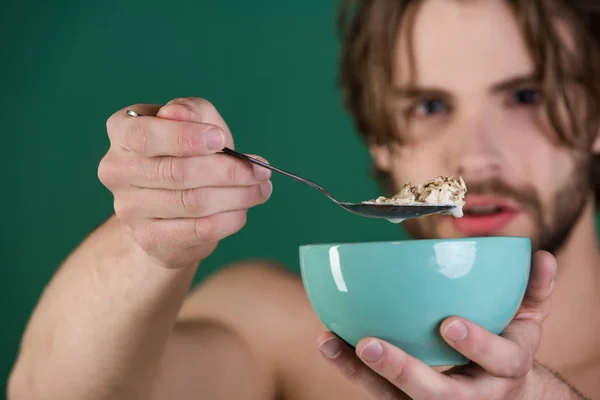 El desayuno. Guapo barbudo joven desayunando sano. Hombre desayunando con cuchara. Hombre comiendo cereales para desayunar. Joven guapo desayunando sano —  Fotos de Stock